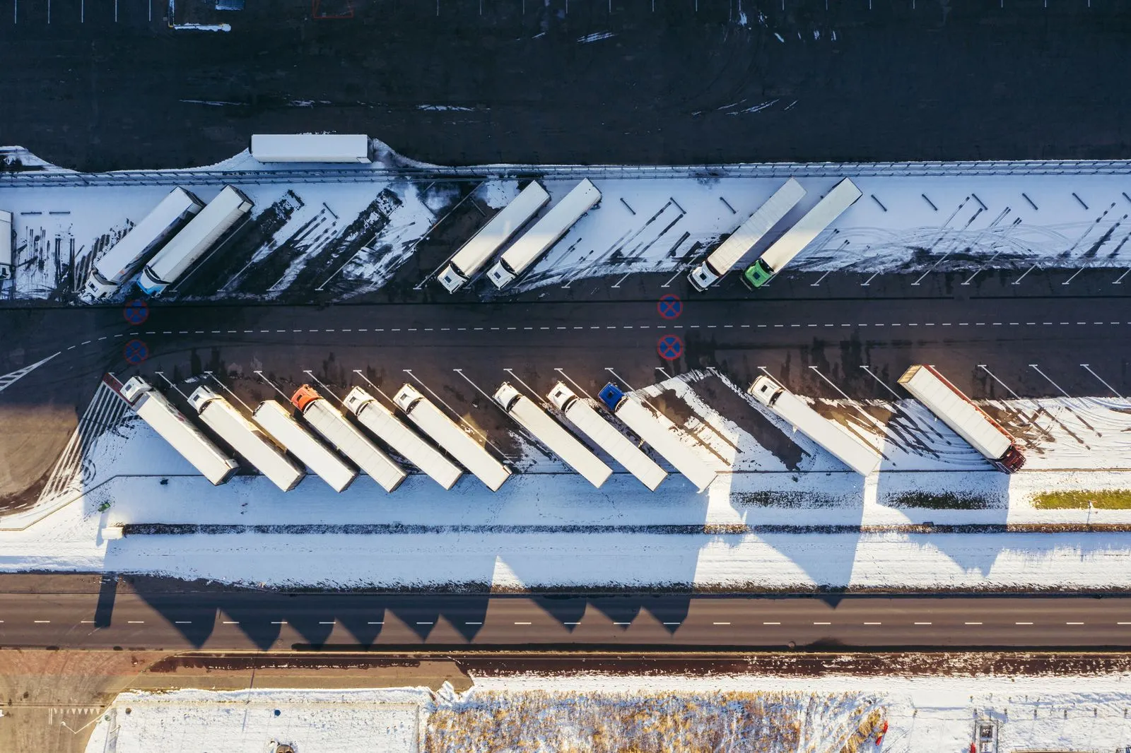 Verschneiter Gewerbehof aus der Luft: geräumte Fahrspuren zwischen schneebedeckten Stellflächen mit abgestellten Lkw.