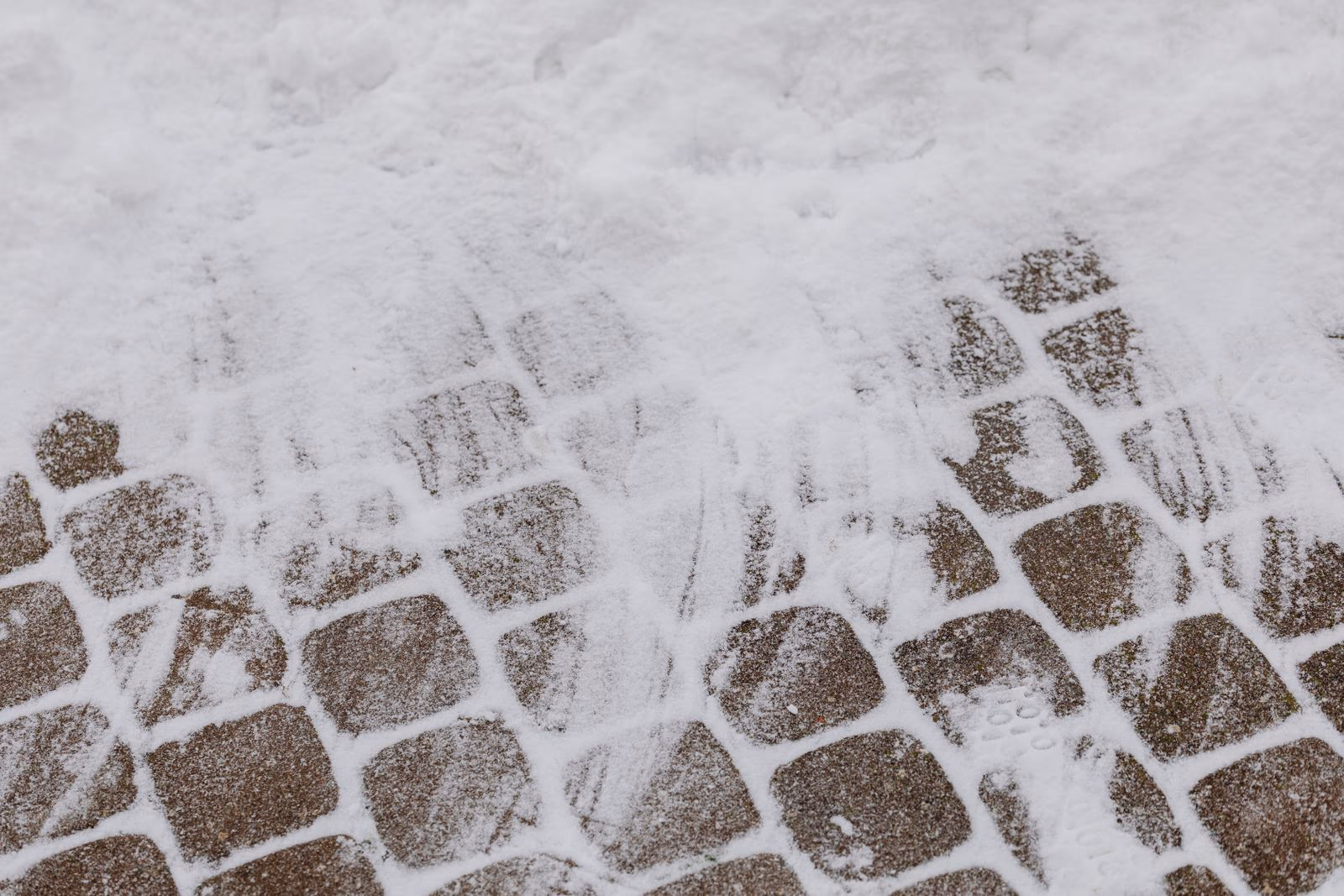 Verschneiter Weg aus Pflastersteinen im Winter mit Fußspuren im frischen Schnee.