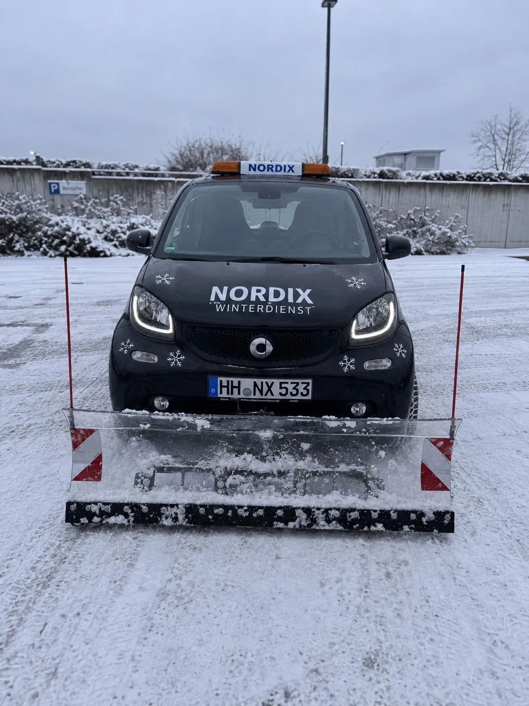 Schwarzer Smart Fortwo von Nordix Winterdienst mit Kennzeichen HH·NX 533 und Räumschild im Schnee.