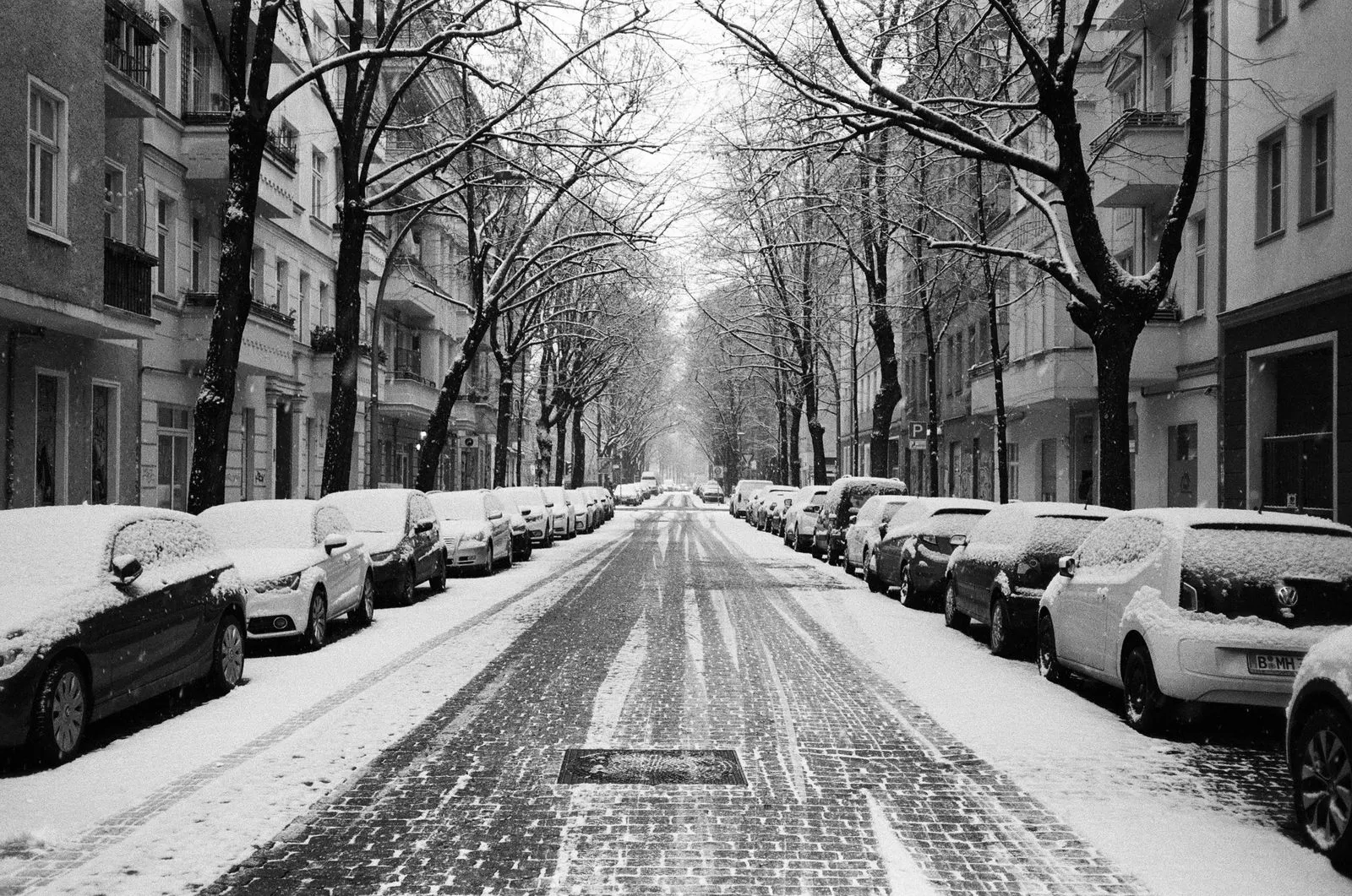 Verschneite Wohnstraße mit Altbauten; die Fahrbahn ist freigefahren, die Randstreifen liegen unter Schnee.