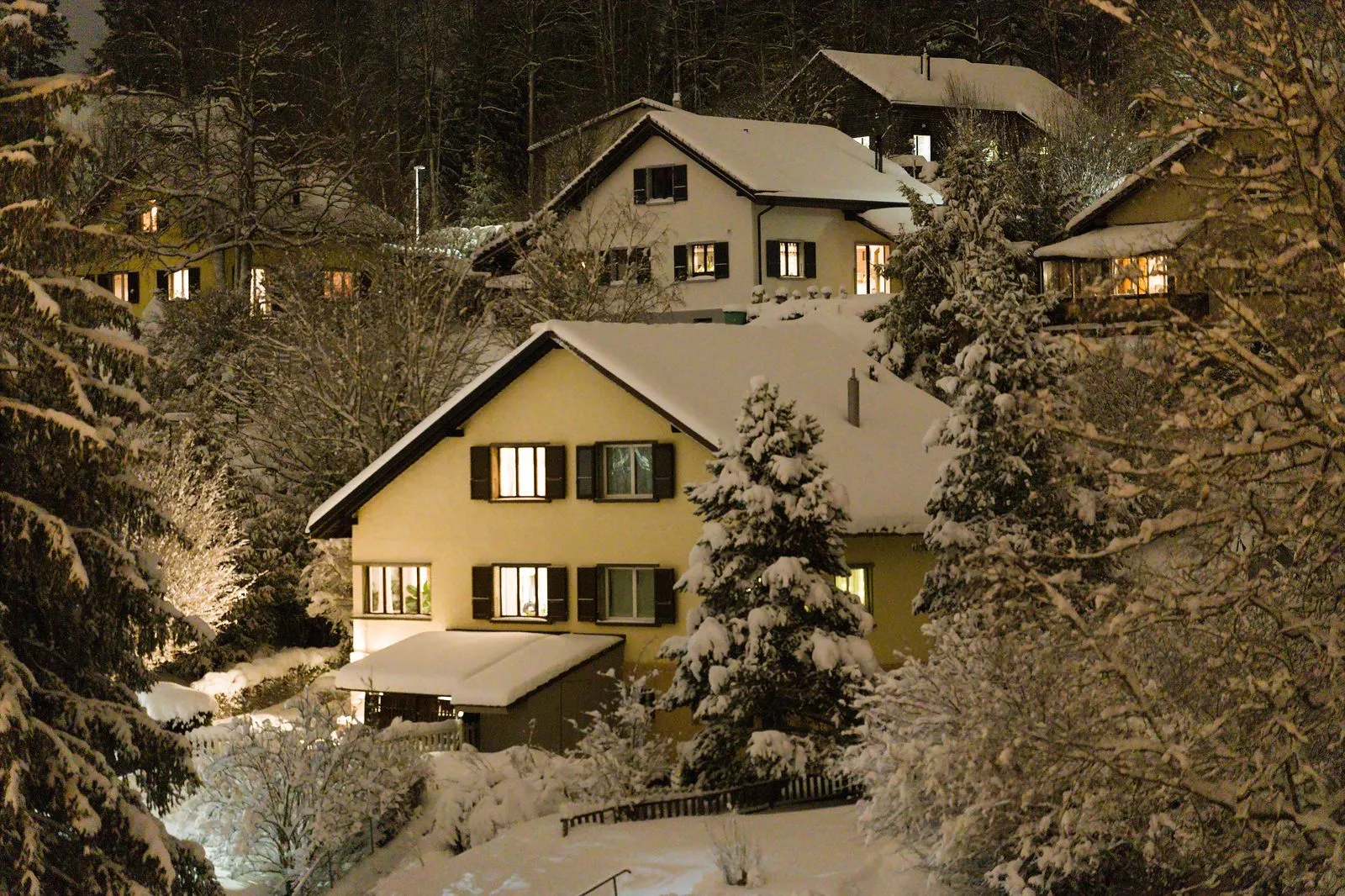 Verschneite Wohnhäuser am Abend mit warm erleuchteten Fenstern.